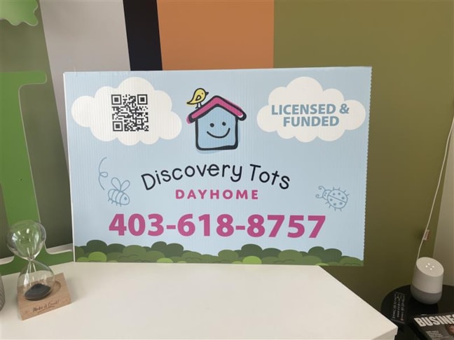 Yard Signs | Bright, bold, and full of smiles — Discovery Tots Dayhome’s new yard signs feature their happy house logo, a quick-scan QR code, and a clear “Funded and Licensed” message on a vibrant blue background.