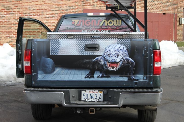 Truck tailgate with image applied to look like tailgate is off and there is a menacing alligator looking back at you.