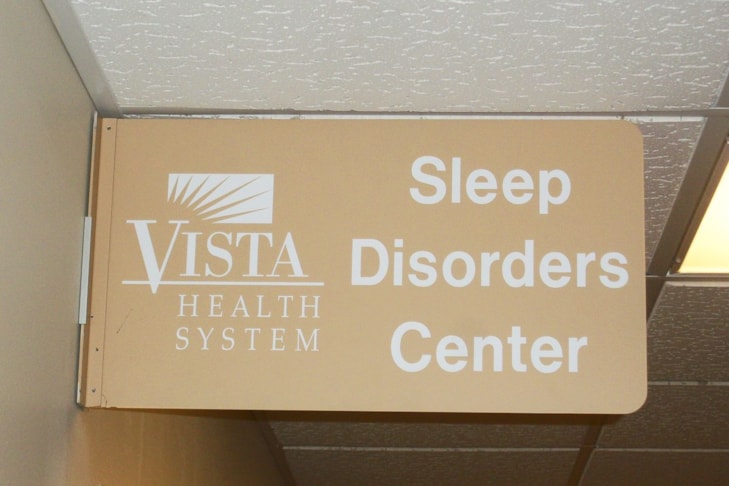 Wayfinding sign mounted to wall above door in hospital